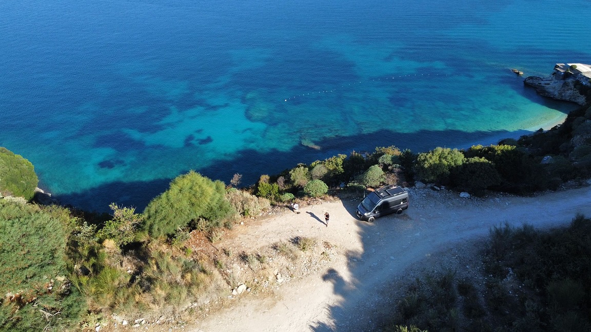 One of our campervans parked above a turquoise cove on the Albanian coast